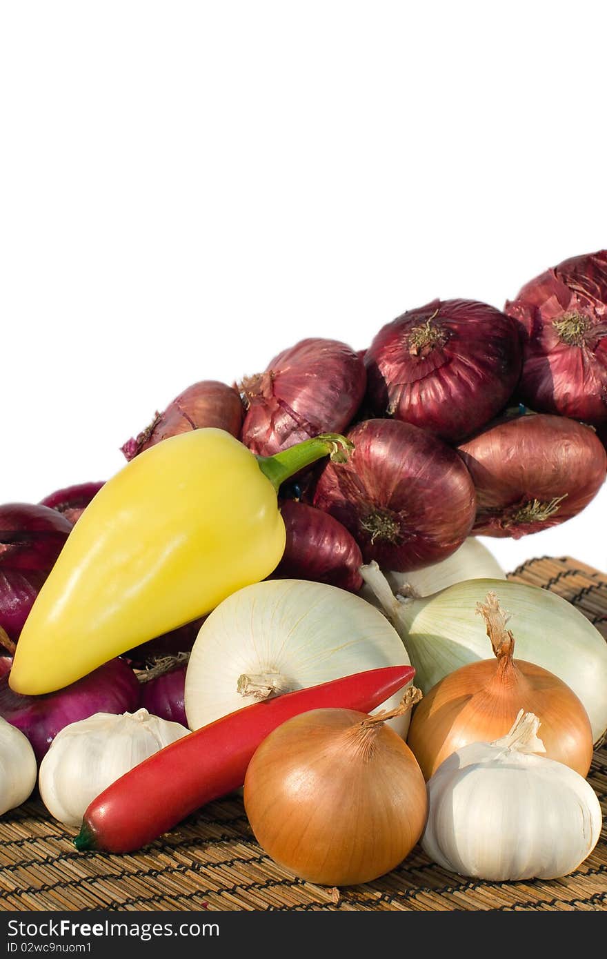 Vegetables - red ,white and yellow onions, hot red pepper,sweet pepper and garlic on a bamboo mat. White background. Vegetables - red ,white and yellow onions, hot red pepper,sweet pepper and garlic on a bamboo mat. White background