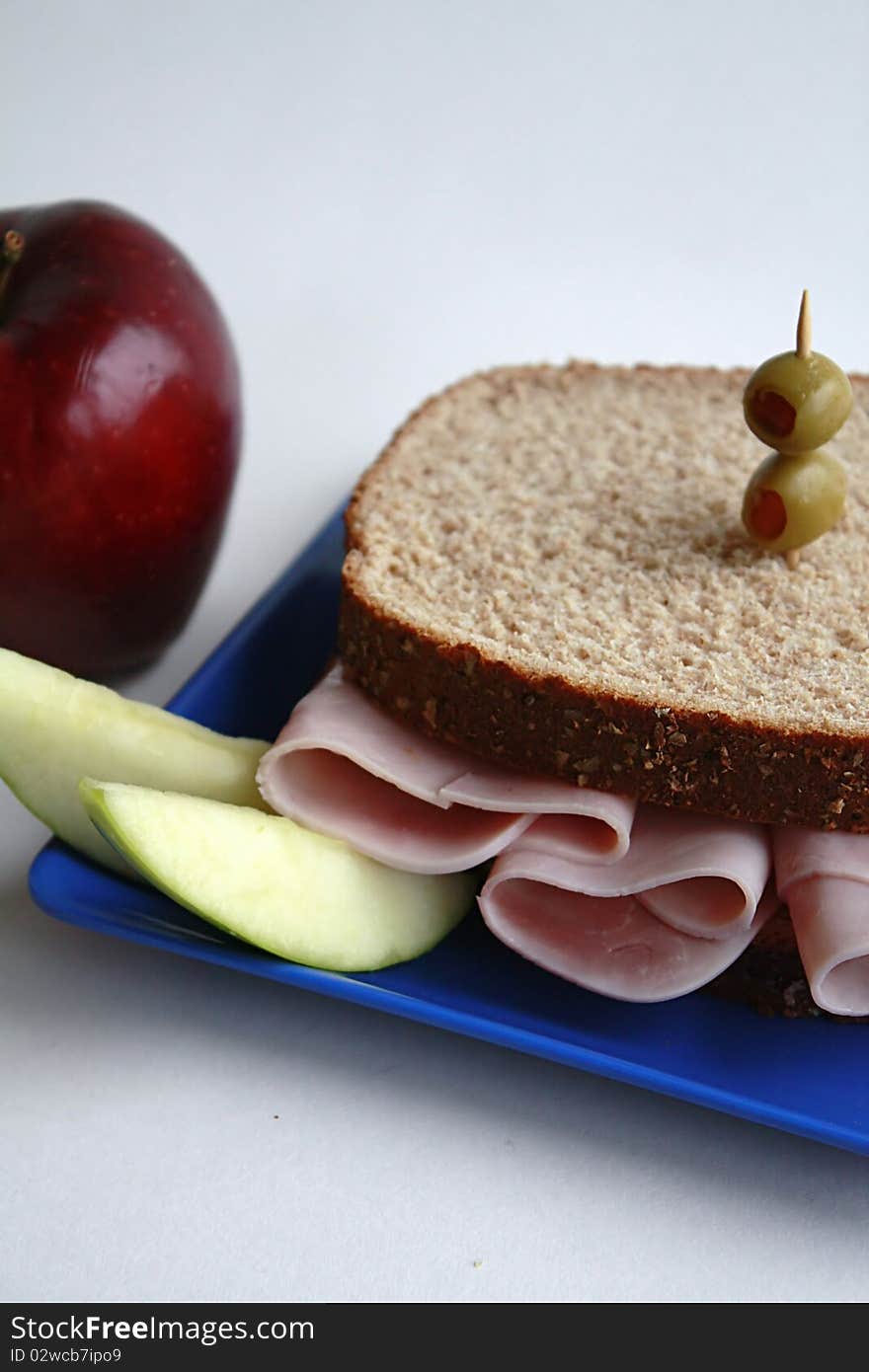 Ham sandwich on whole wheat bread garnished with olives and apple slices.