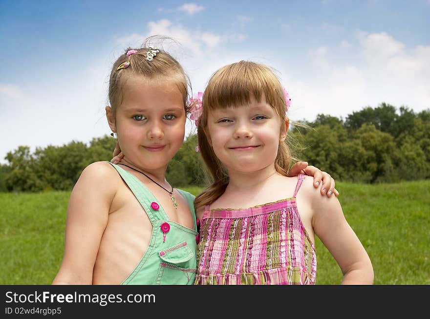 Two little girls in the summer park (one with closed eyes from bright light). Two little girls in the summer park (one with closed eyes from bright light)