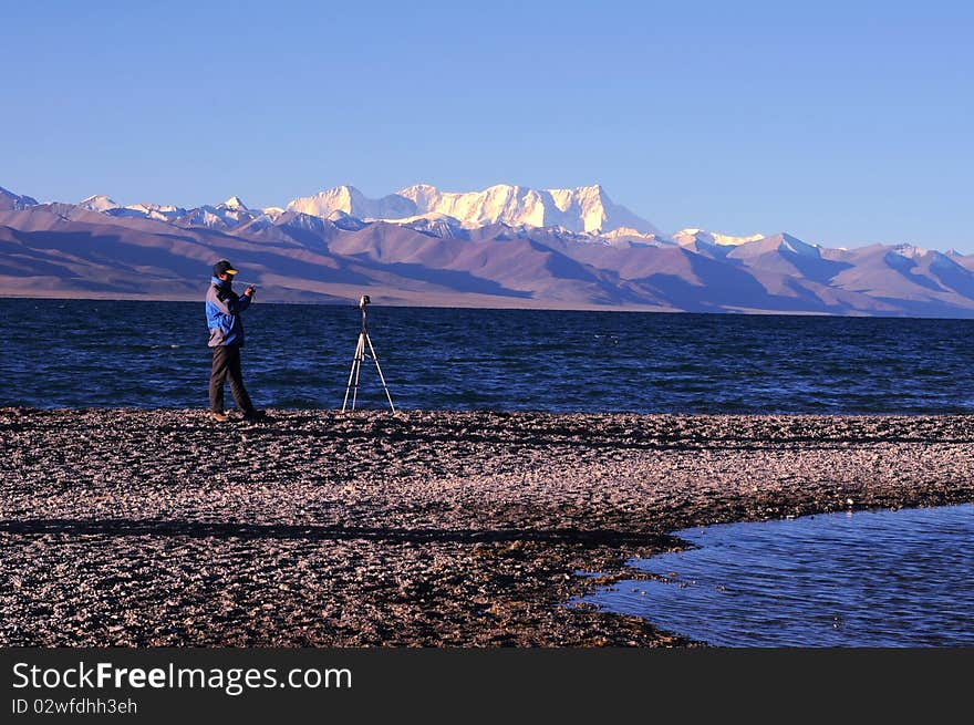 Portrait of a photographer shooting at sunrise at the bank of a blue lake in Tibet.