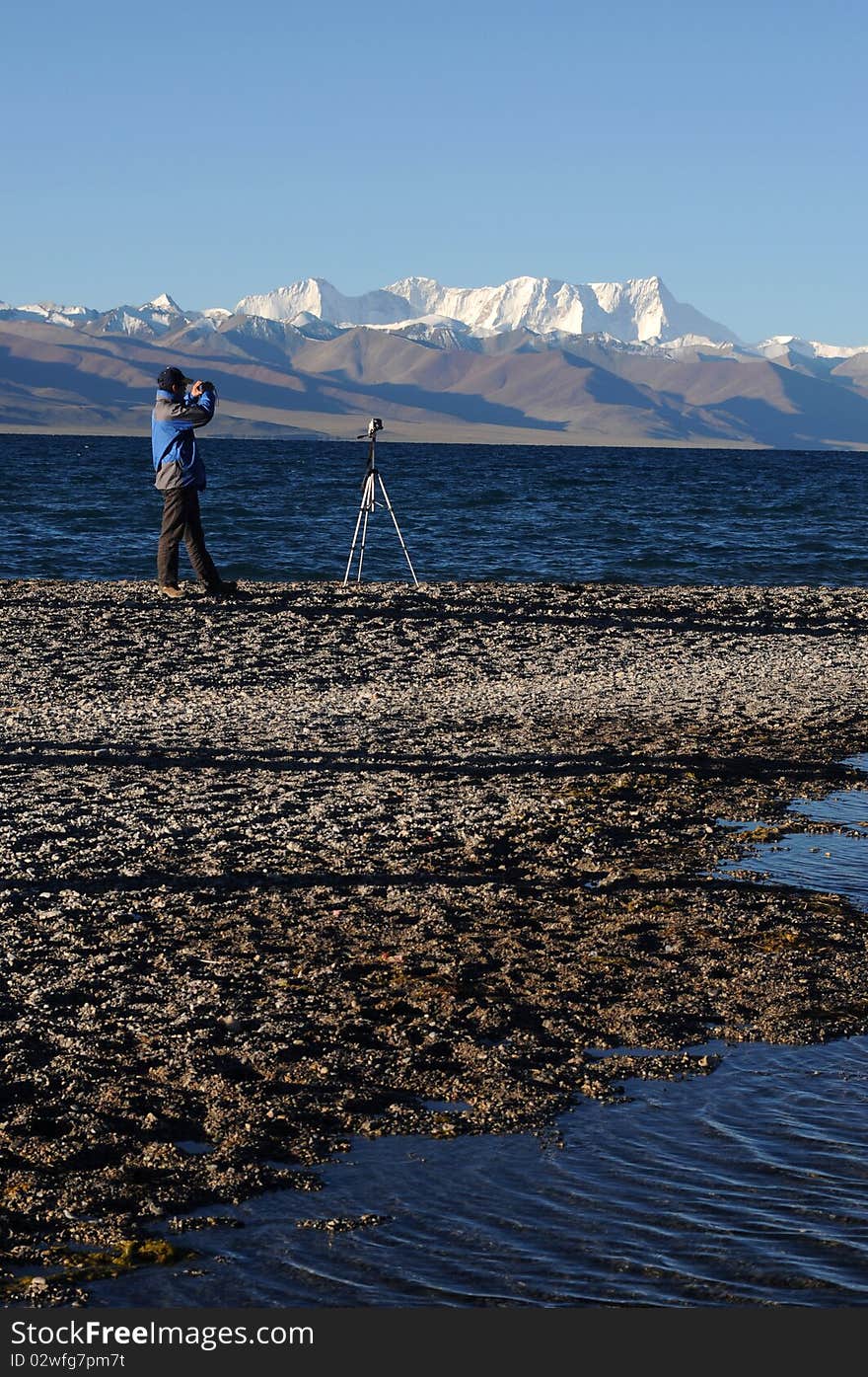 Portrait of a photographer shooting at sunrise at the bank of a blue lake in Tibet.