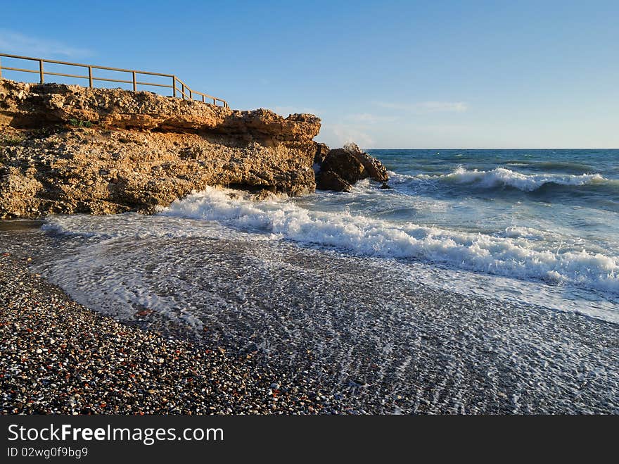 Late afternoon shot of a secluded beach spot at the Costa del Sol. Waves come rolling onto the colourful stone beach as tranquility sets in after the day's vibrant beach life.