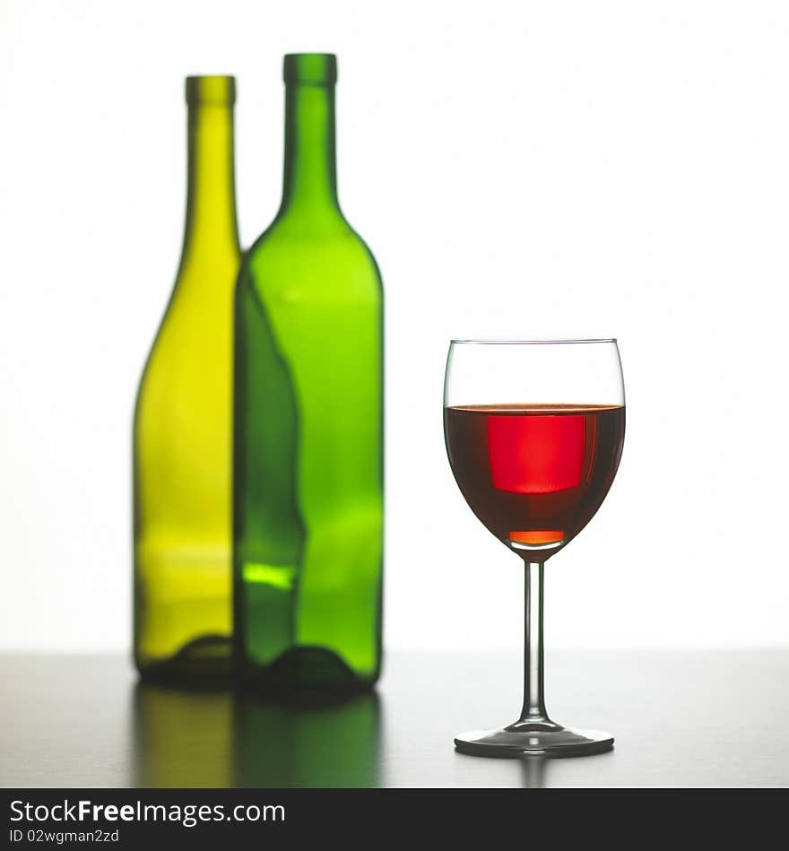 glass of red wine with two green wine bottles