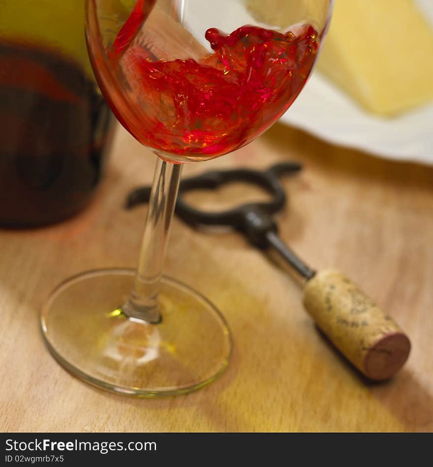 Close up of red rose wine poured into glass next to plate of cheese and corkscrew