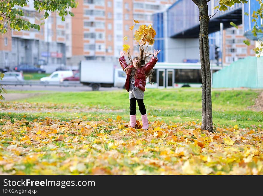 Adorablesmall girl with long dark hair in colorful clothers has fun in sunny autumn day in the park with yellow leaves. Adorablesmall girl with long dark hair in colorful clothers has fun in sunny autumn day in the park with yellow leaves