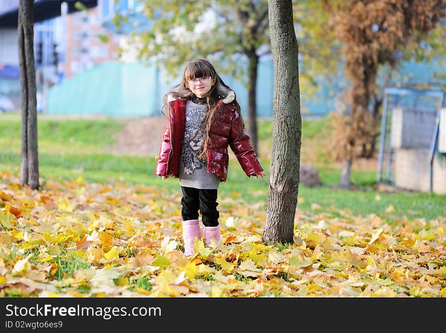 Adorablesmall girl with long dark hair in colorful clothers has fun in sunny autumn day in the park with yellow leaves. Adorablesmall girl with long dark hair in colorful clothers has fun in sunny autumn day in the park with yellow leaves