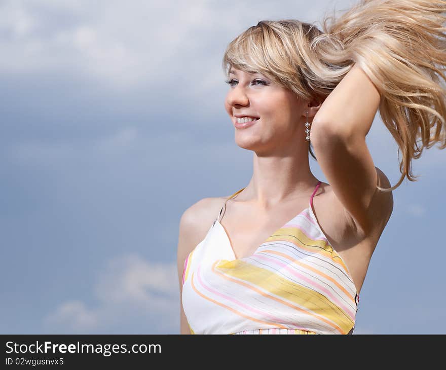 Outdoor portrait of a young lady on a blue cloudy sky background. Outdoor portrait of a young lady on a blue cloudy sky background