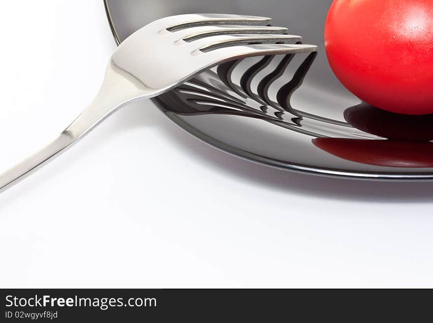 Red tomato on a black high-gloss plate with stainless fork. Red tomato on a black high-gloss plate with stainless fork