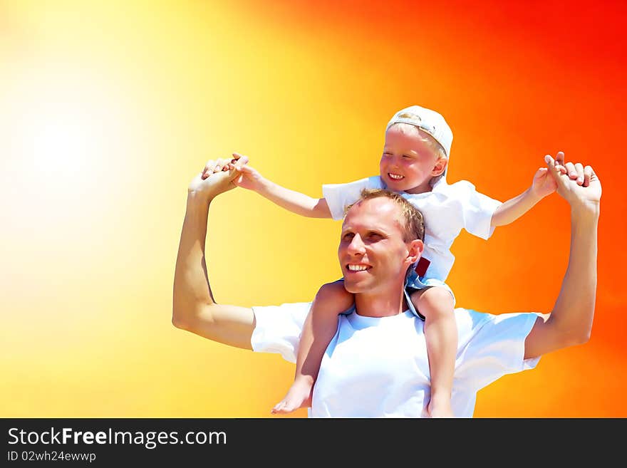 Joyful father giving piggyback ride to his son against a sky background. Joyful father giving piggyback ride to his son against a sky background