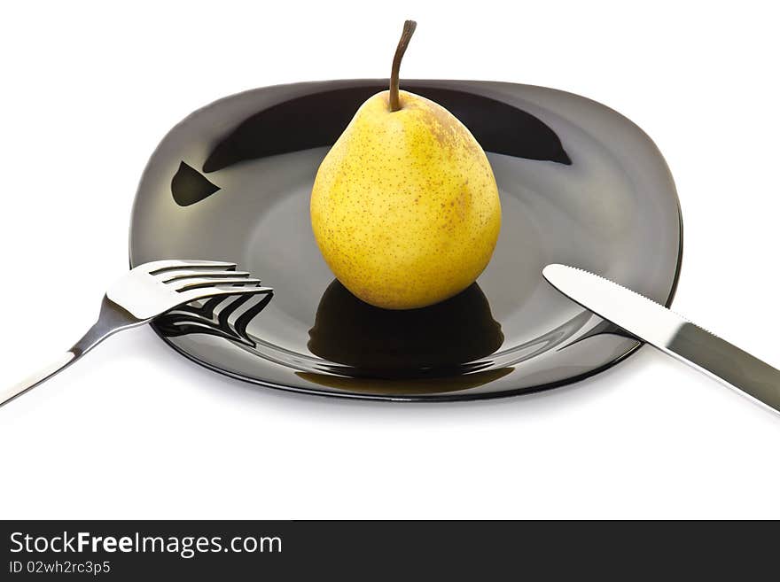 Fresh yellow pear on a black plate with fork and knife