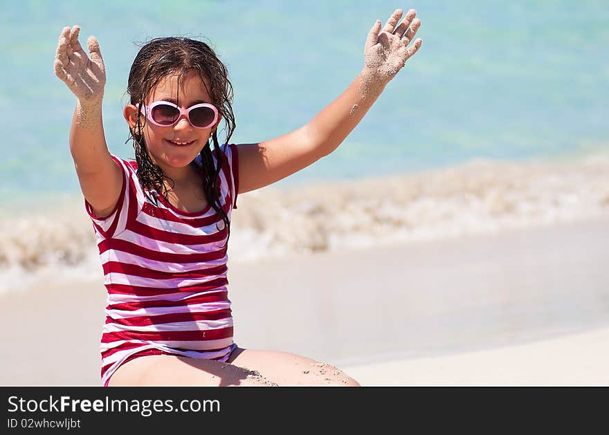 Girl with sunglasses sitting in the sand on a beac