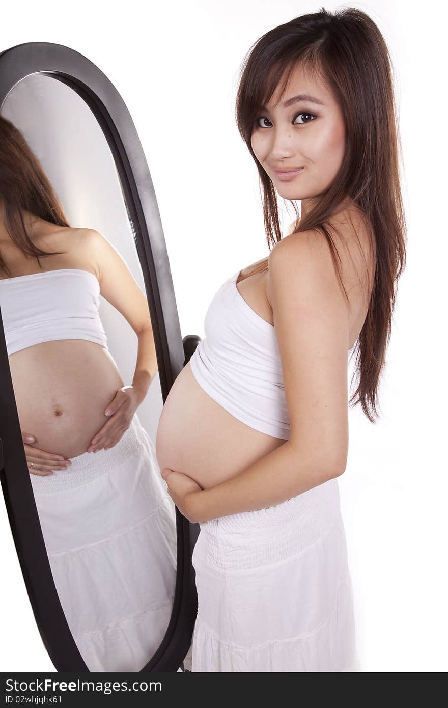 A woman in white with her belly showing is standing by a mirror. A woman in white with her belly showing is standing by a mirror.