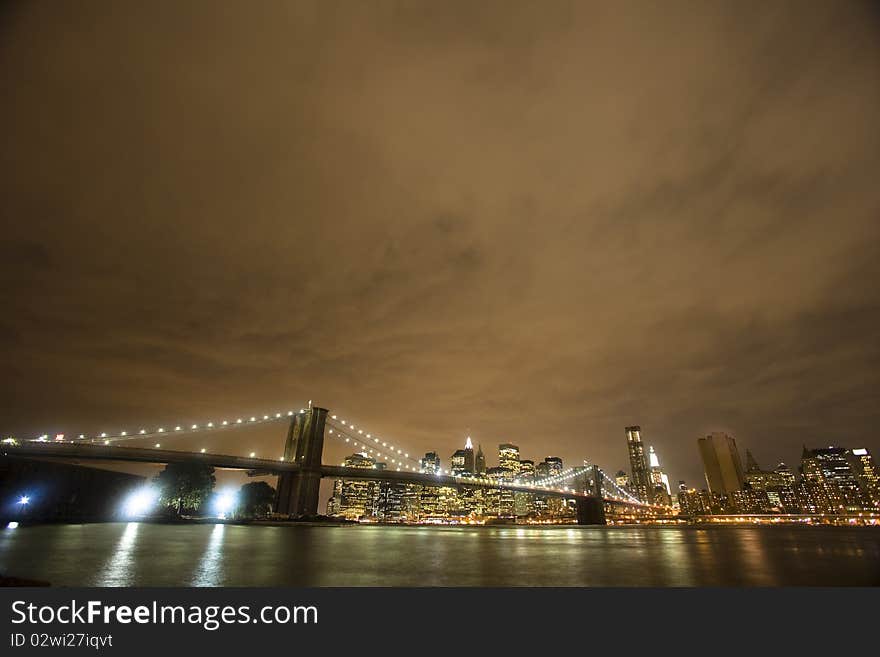 The iconic Brooklyn Bridge stretches across the East River on a cloudy evening. The iconic Brooklyn Bridge stretches across the East River on a cloudy evening