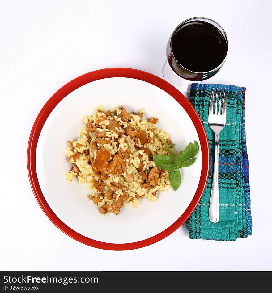 Risotto with mushrooms on a plate decorated with basil, glass of red wine and a fork on a napkin