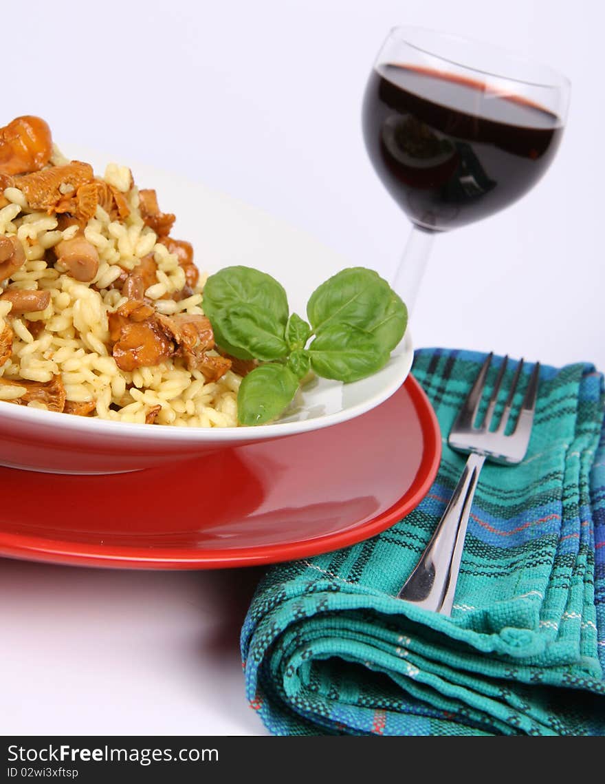 Risotto with mushrooms on a plate decorated with basil, glass of red wine and a fork on a napkin, in close up