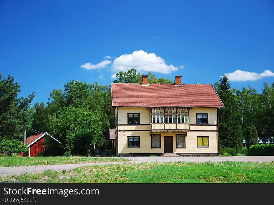 Typical building is in the green yard overgrown with grass. In the background there are summer forest and the blue sky. The estate has access asphalt road. Typical building is in the green yard overgrown with grass. In the background there are summer forest and the blue sky. The estate has access asphalt road