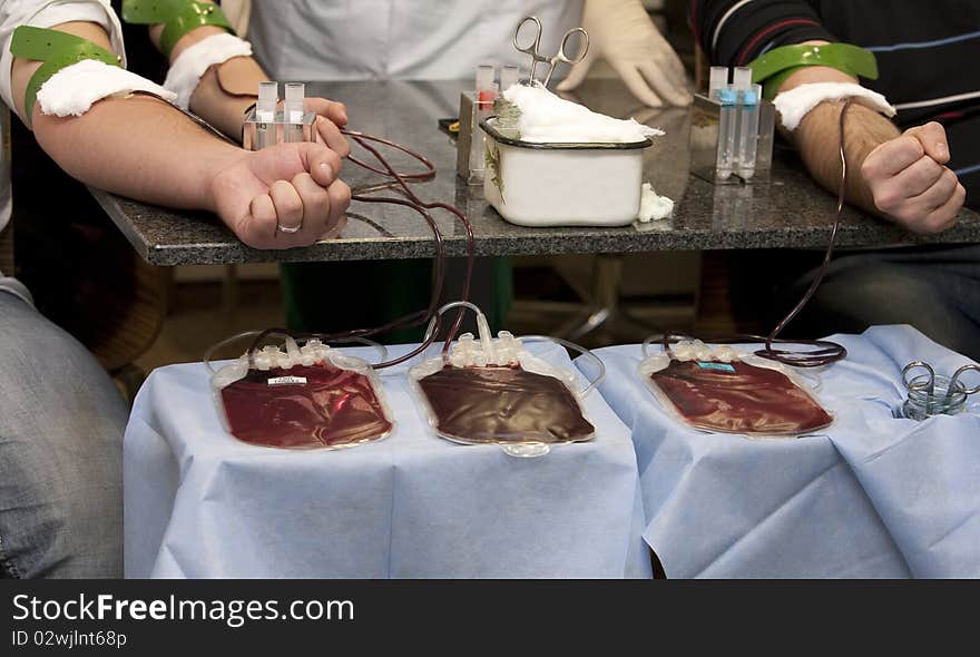 Blood donation, hands with rubber tourniquet used in blood draw procedures. blood bags on the table