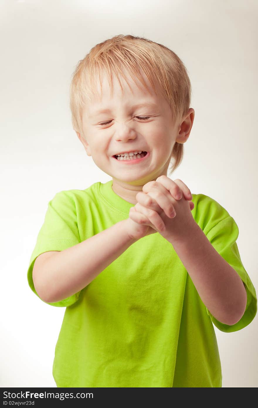 Boy smiled, his eyes shut, hands folded, on a gray background. Boy smiled, his eyes shut, hands folded, on a gray background