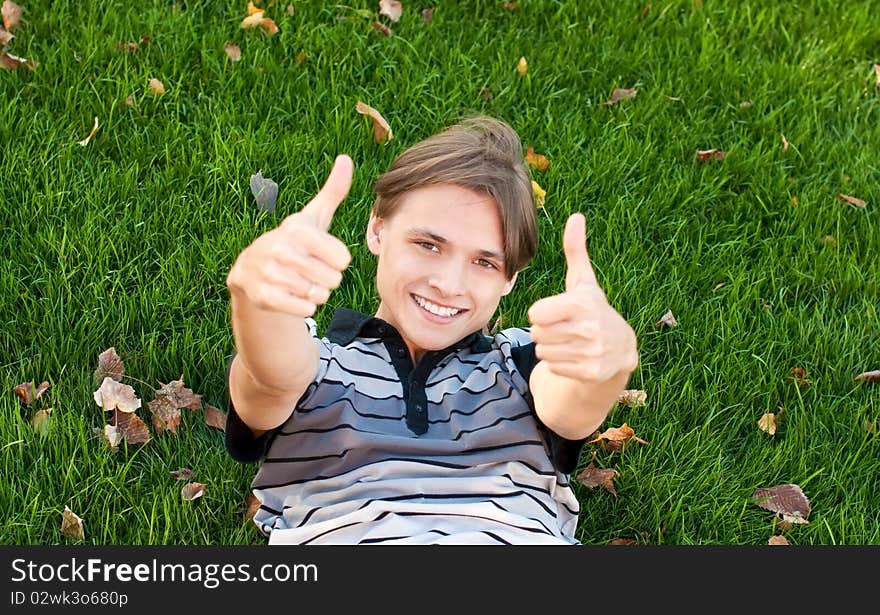 Young man lying on the grass with thumbs up. Young man lying on the grass with thumbs up