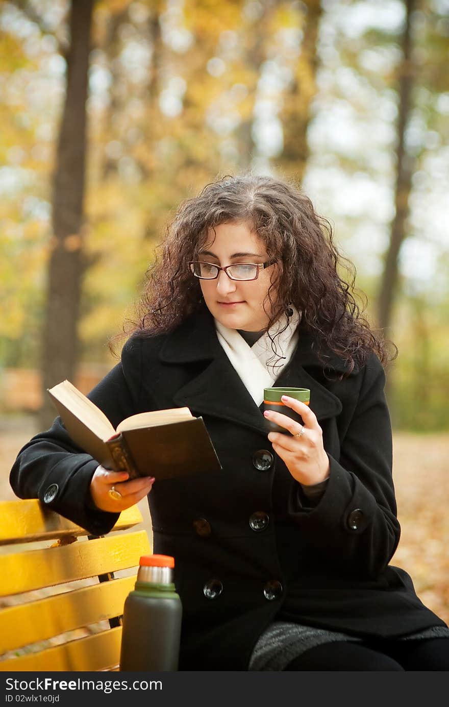 Young woman reading book and drinkin coffee on bench