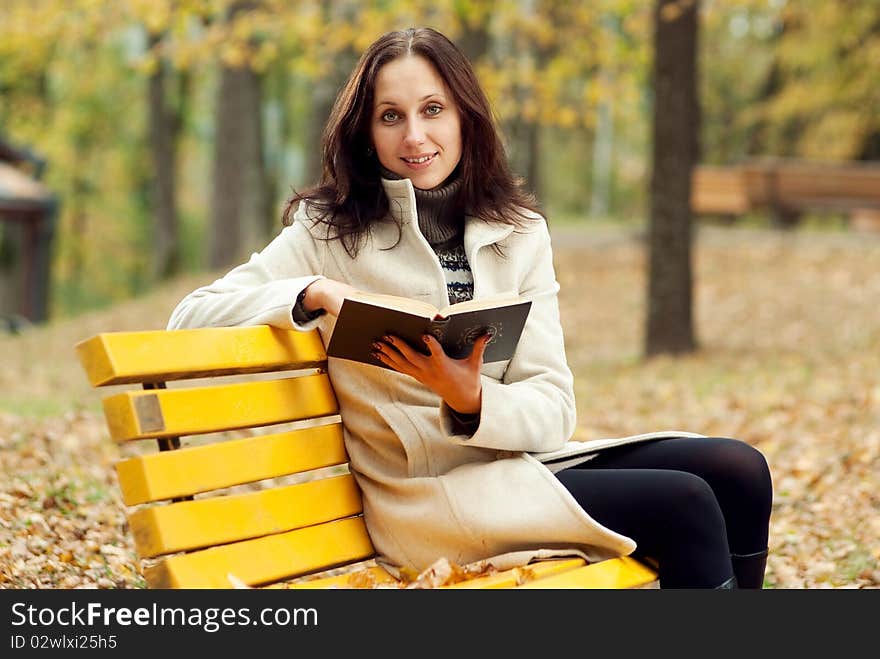 Young woman sitting on bench in autumn park