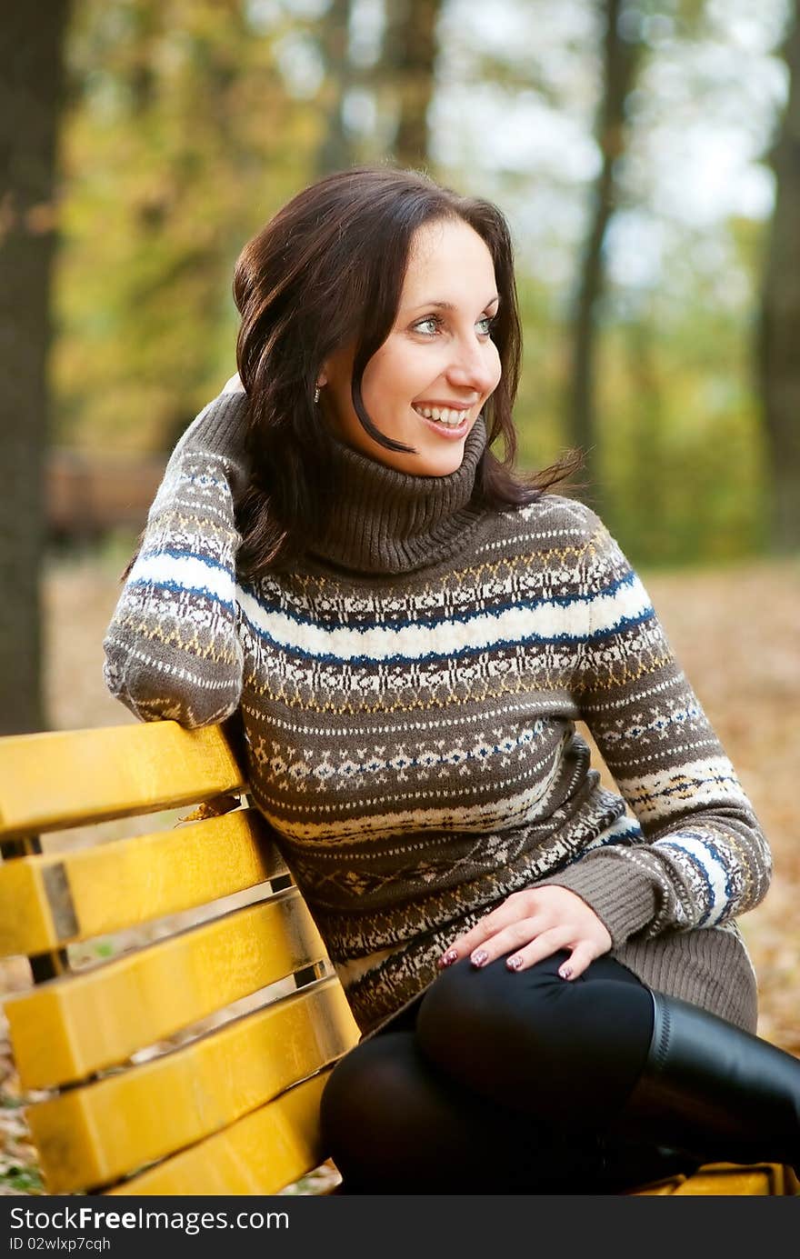 Young woman sitting on bench and smiling in autumn park