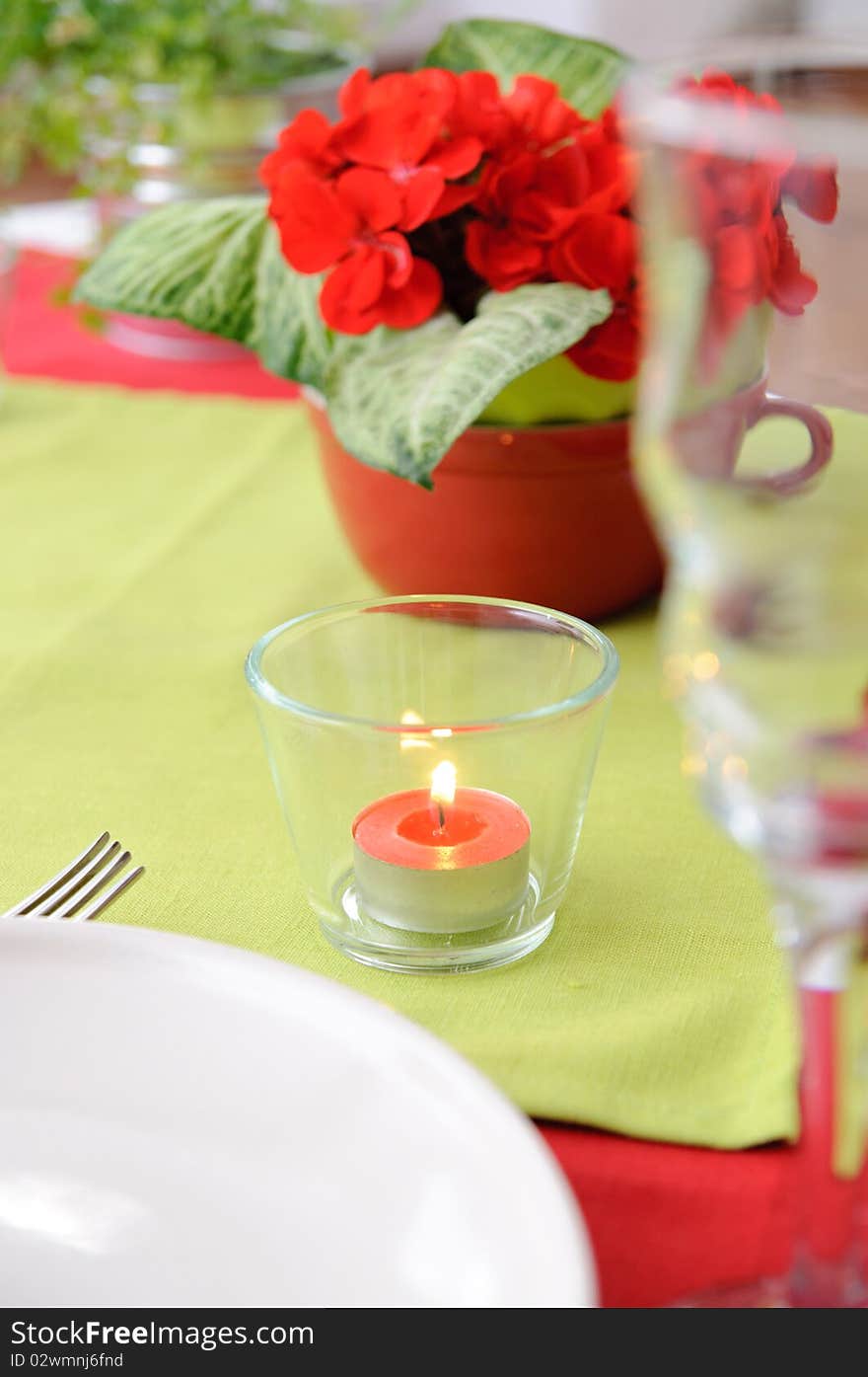 Red candle in a glass candlestick and flowers on the table in red and green colors