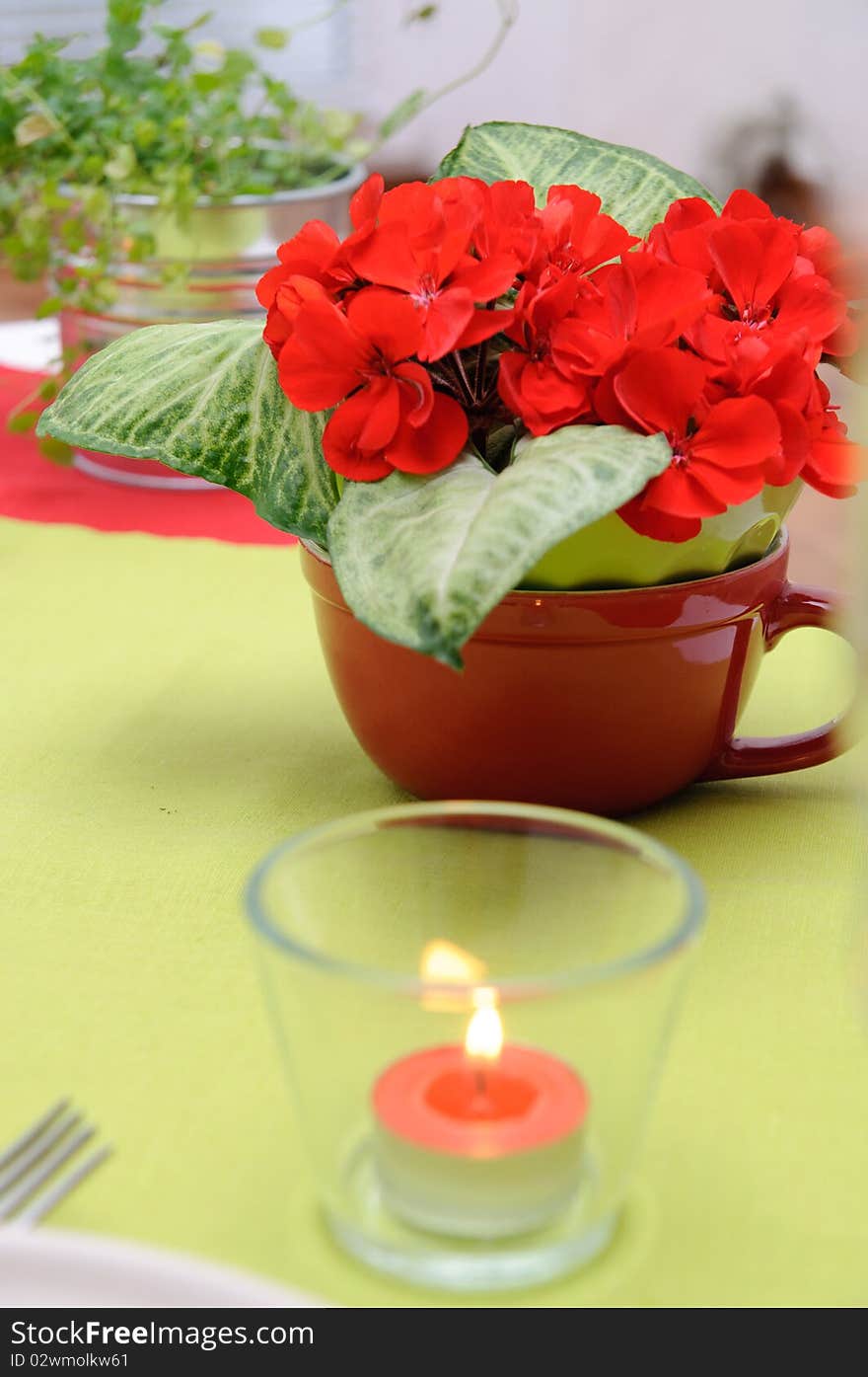 Red candle in a glass candlestick and flowers on the table in red and green colors