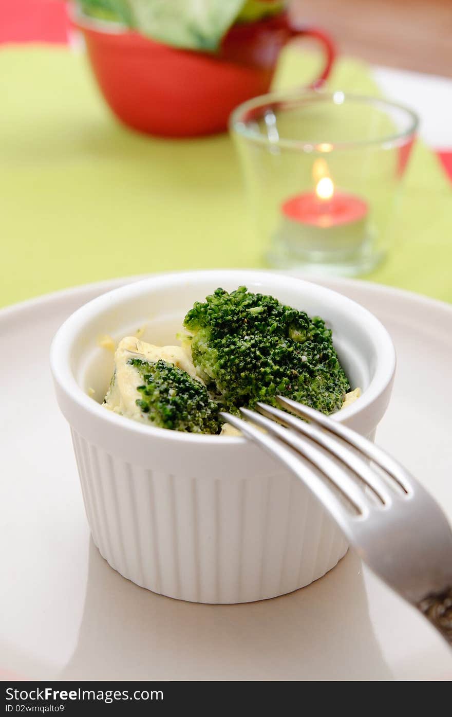 Omelet with broccoli in a white ceramic pot, and candles on the table in red and green colors