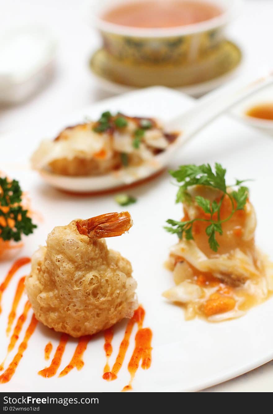 A plate of mixed Chinese delicacies, placed on a white plate and having also soup and sauces on the background.