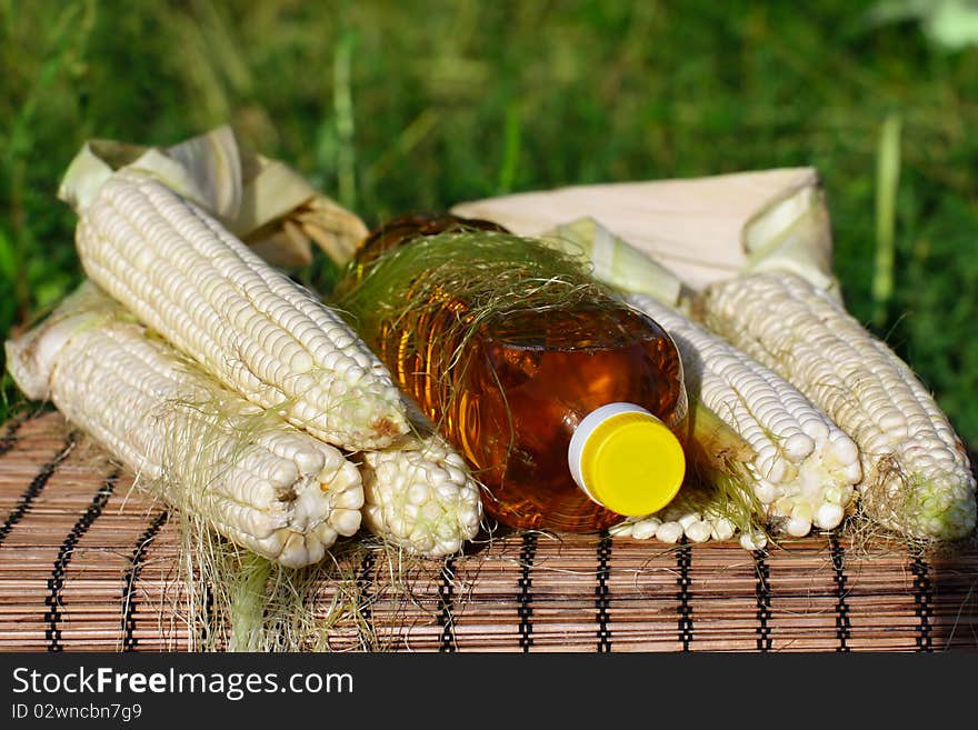 Freshlpicked corn on the cob and bottle of yellow oil. Freshlpicked corn on the cob and bottle of yellow oil.