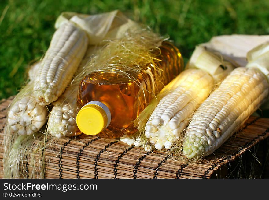 Freshlpicked corn on the cob and bottle of yellow oil. Freshlpicked corn on the cob and bottle of yellow oil.