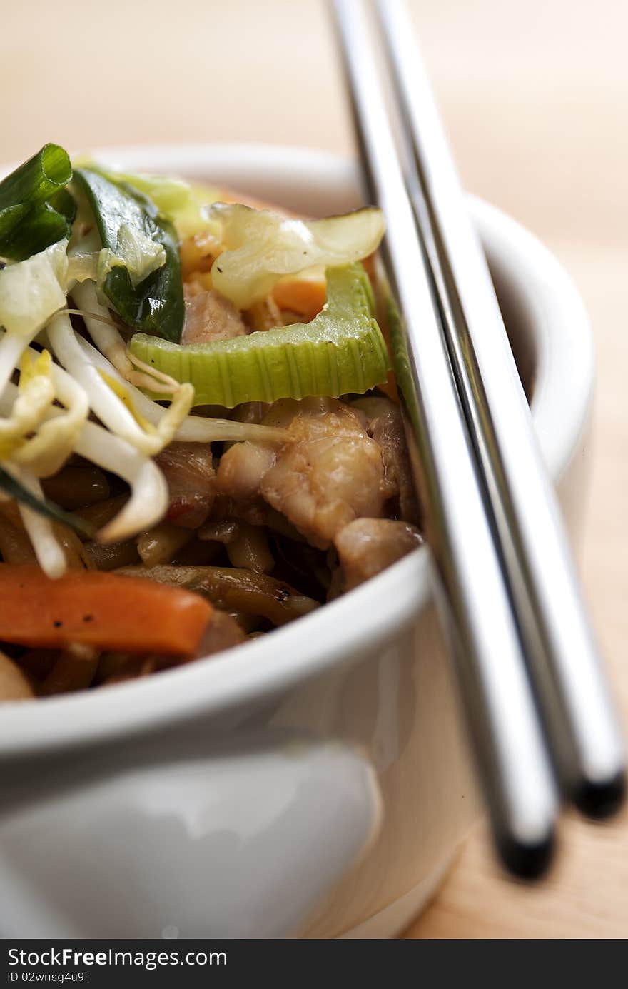 Close up shot of a bowl of asian stir fried noodles with chicken, celery, carrots, and bean sprouts on a wooden surface. Close up shot of a bowl of asian stir fried noodles with chicken, celery, carrots, and bean sprouts on a wooden surface