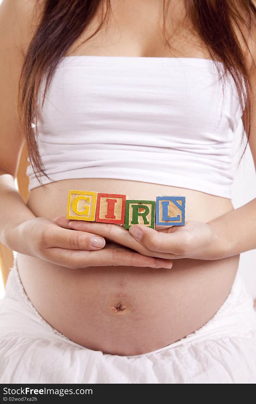 A pregnant woman is holding some blocks against her stomach that spell girl. A pregnant woman is holding some blocks against her stomach that spell girl