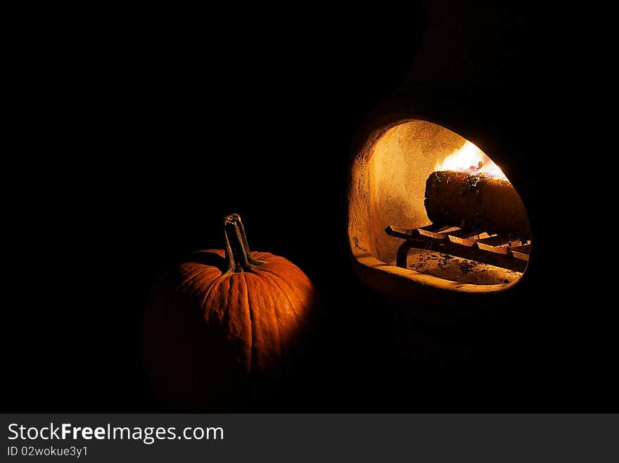 Pumpkin lit by firelight from a chiminea on black background. Pumpkin lit by firelight from a chiminea on black background