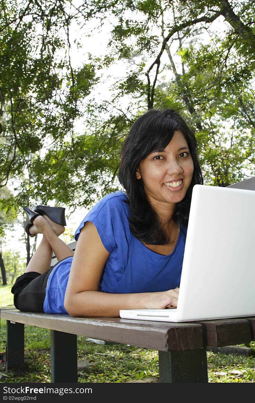 An Asian woman using her laptop on a park bench. An Asian woman using her laptop on a park bench