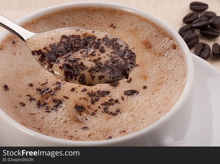 Cappuccino in a white ceramic cup with a saucer and a spoon.