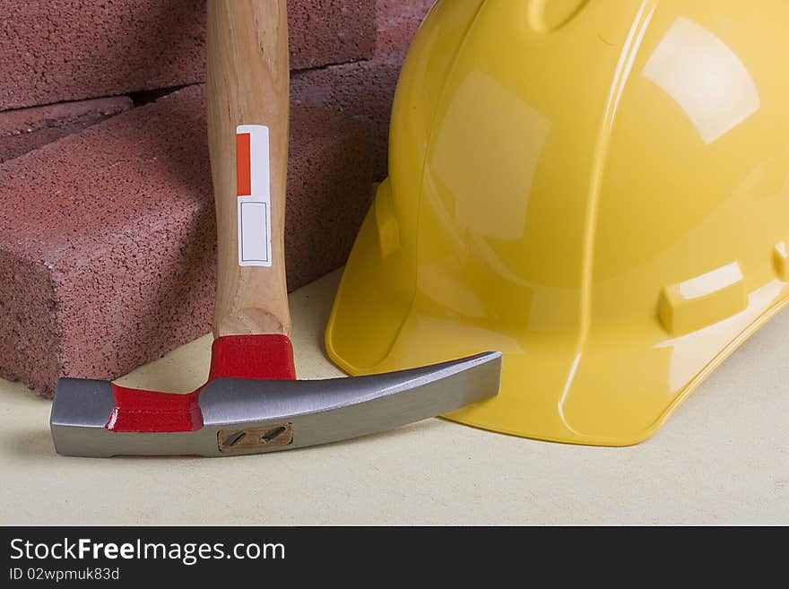 Yellow hard hat next to bricks and a mason's hammer.