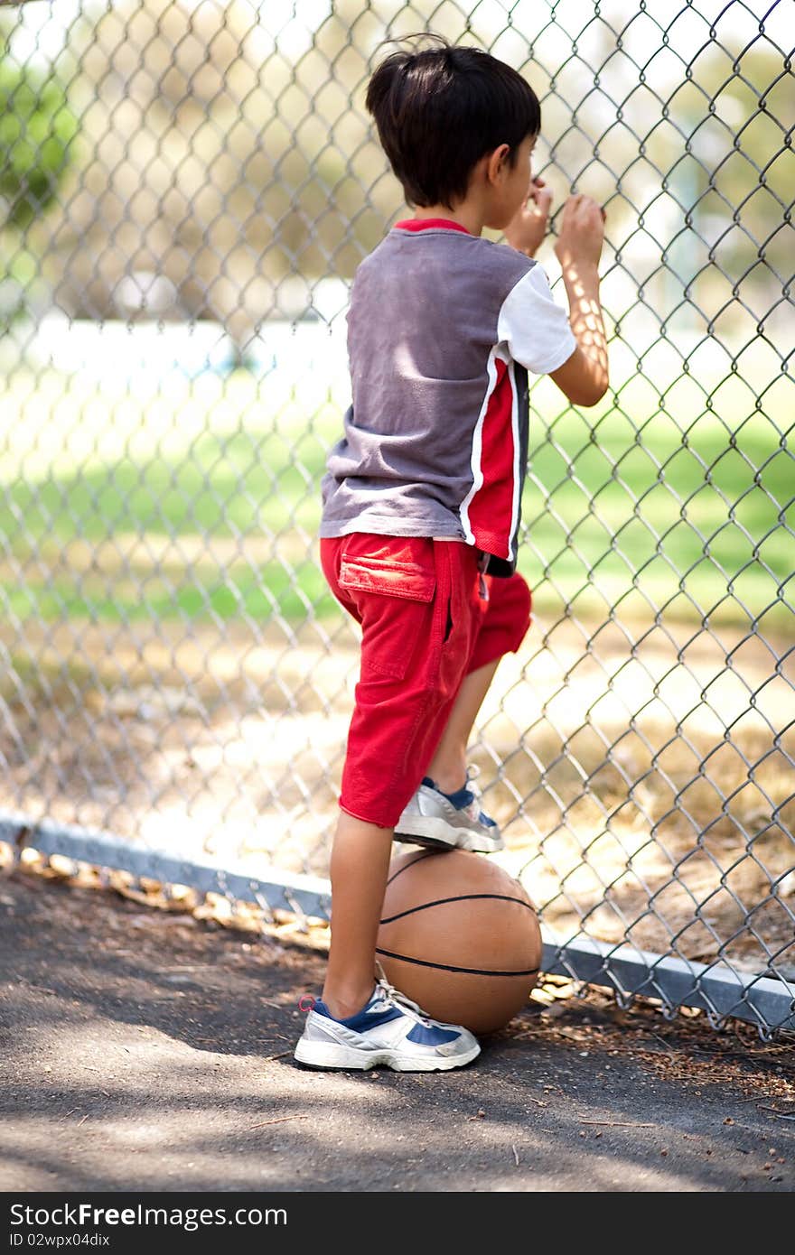 Rear view of young basketball player holding ball under his leg and and looking through fence