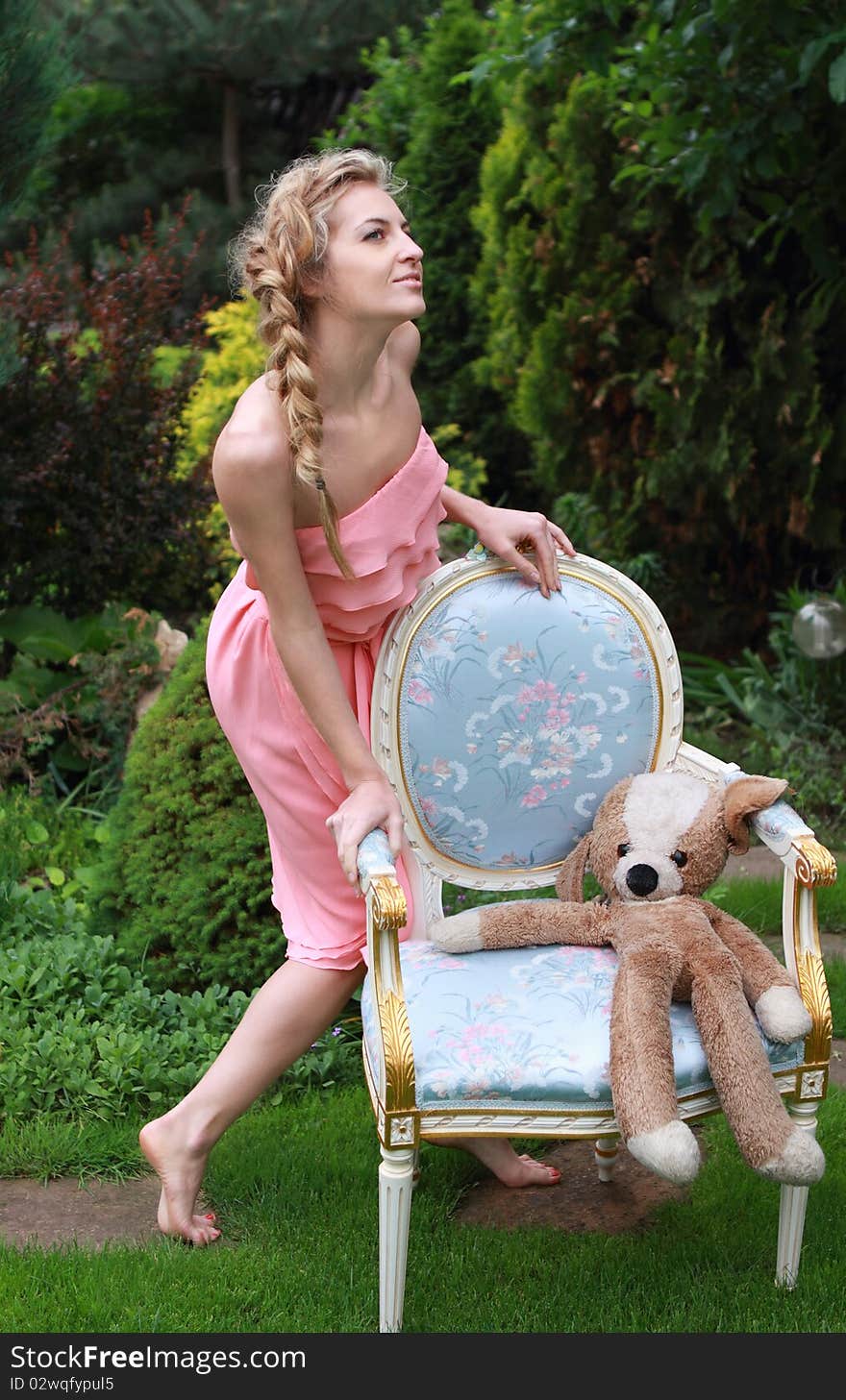 Attractive blond girl in the pink dress with toy in the garden. Attractive blond girl in the pink dress with toy in the garden