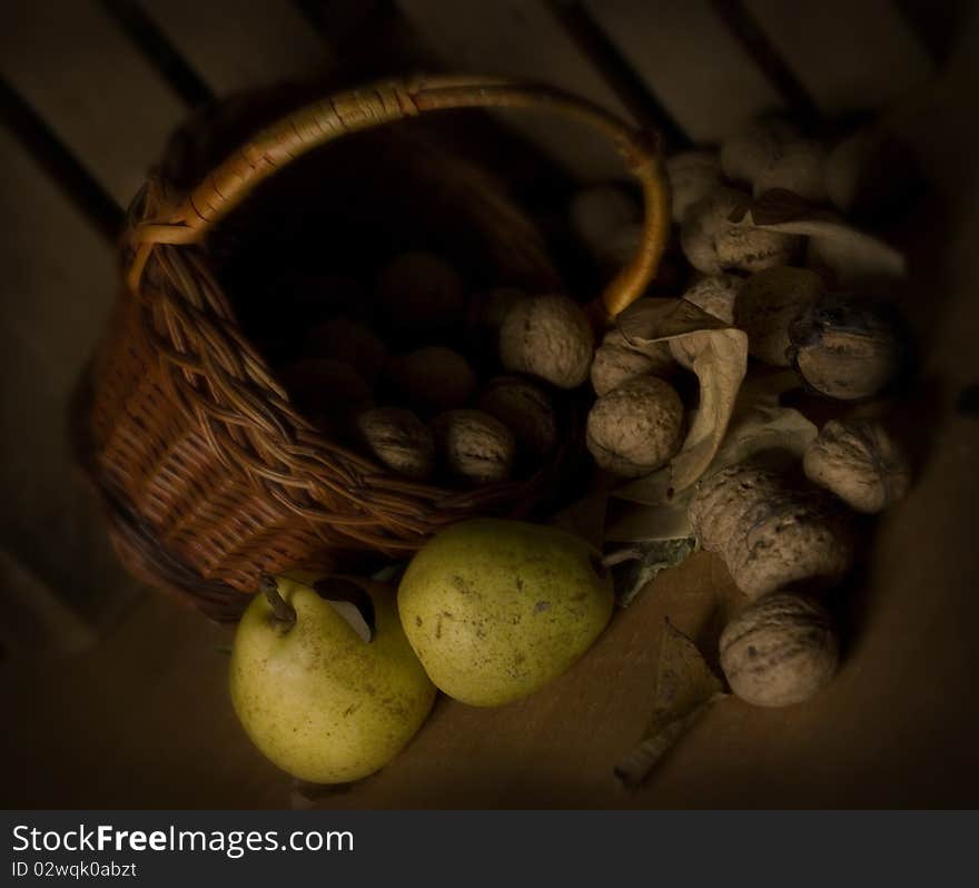 Green pears, nuts and basket against the dark wooden background, dark still life in vintage style. Green pears, nuts and basket against the dark wooden background, dark still life in vintage style