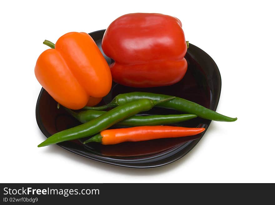 Bell and chilli peppers on black plate, isolated on white background