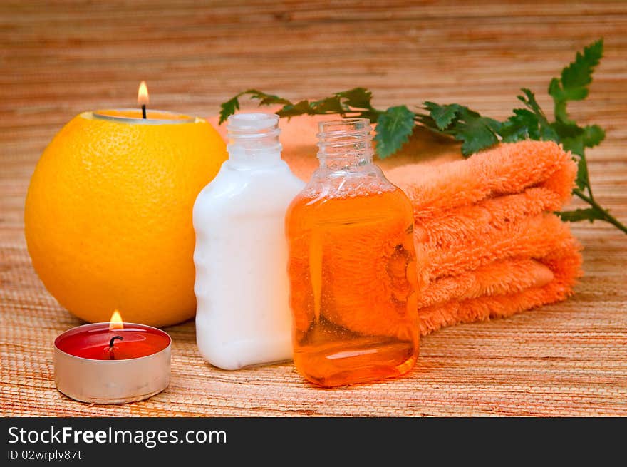 Orange towel, Fern branch and a burning candle in citrus. Orange towel, Fern branch and a burning candle in citrus