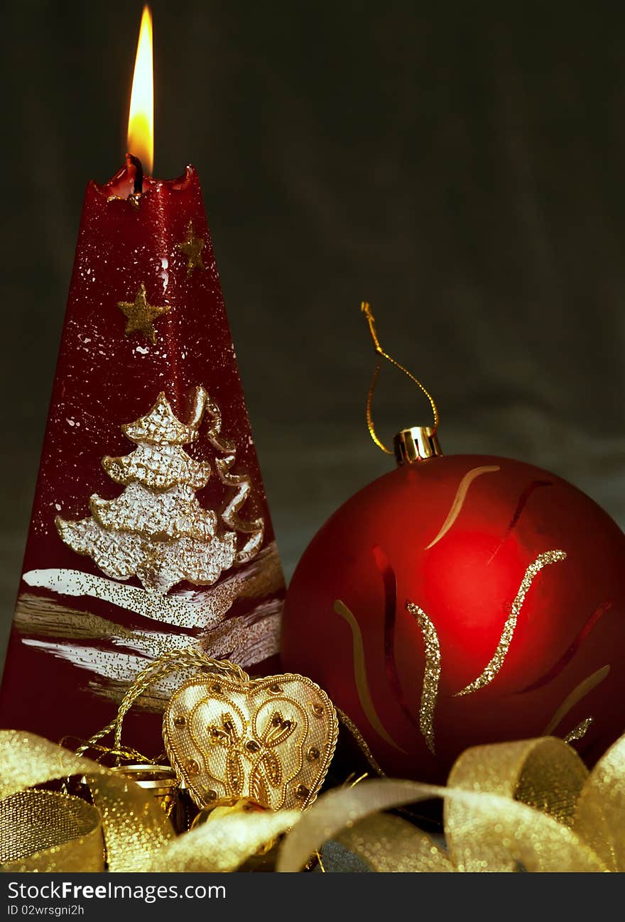 Christmas still life - red burning candle with evening ball and little gold heart on dark green background. Christmas still life - red burning candle with evening ball and little gold heart on dark green background