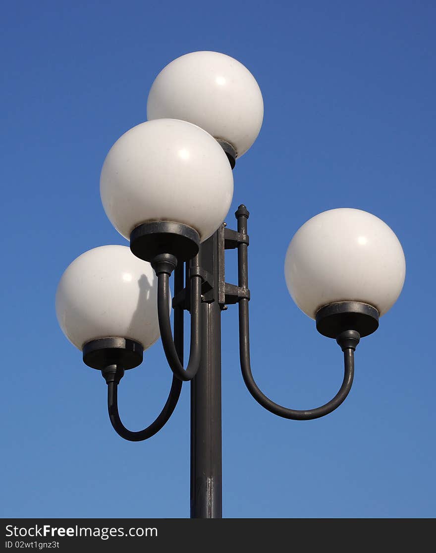 Street  lamp in form of white balls in sunny day on a blue sky background