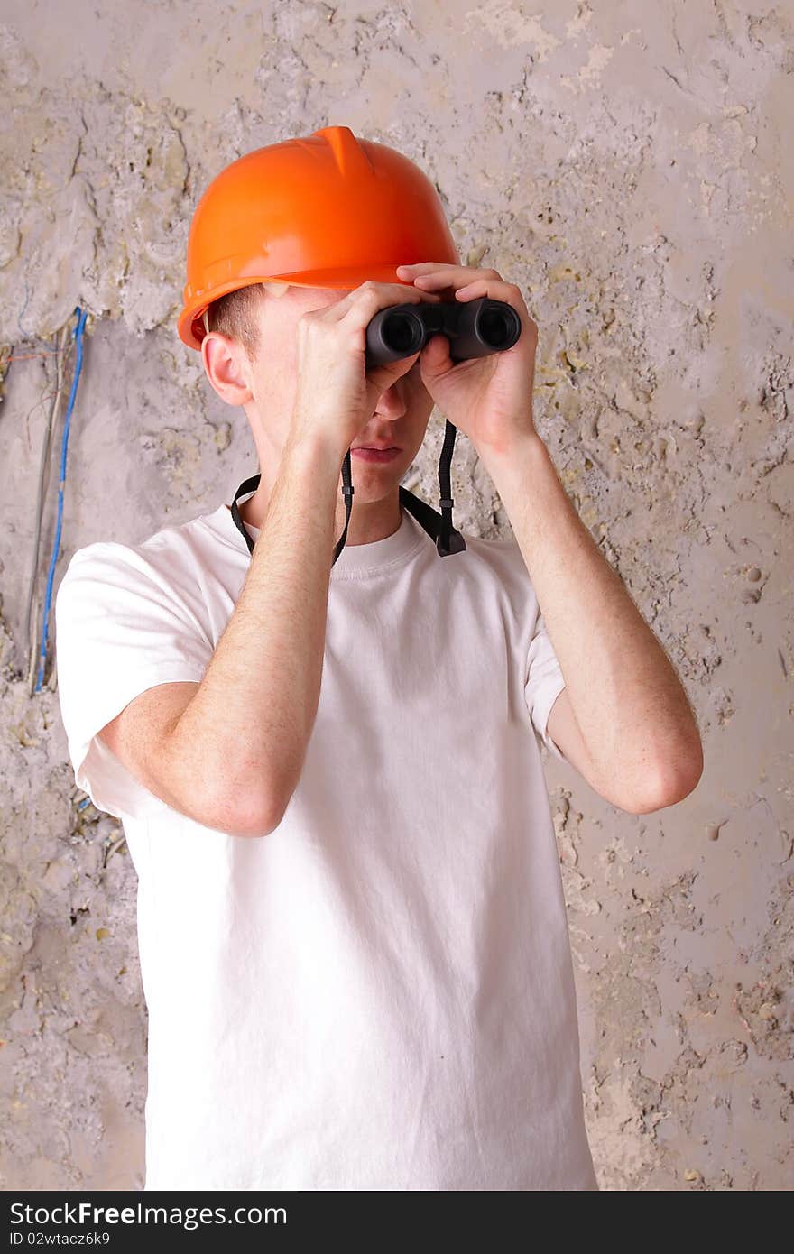 Builder looking through binoculars at the background of the plastered walls