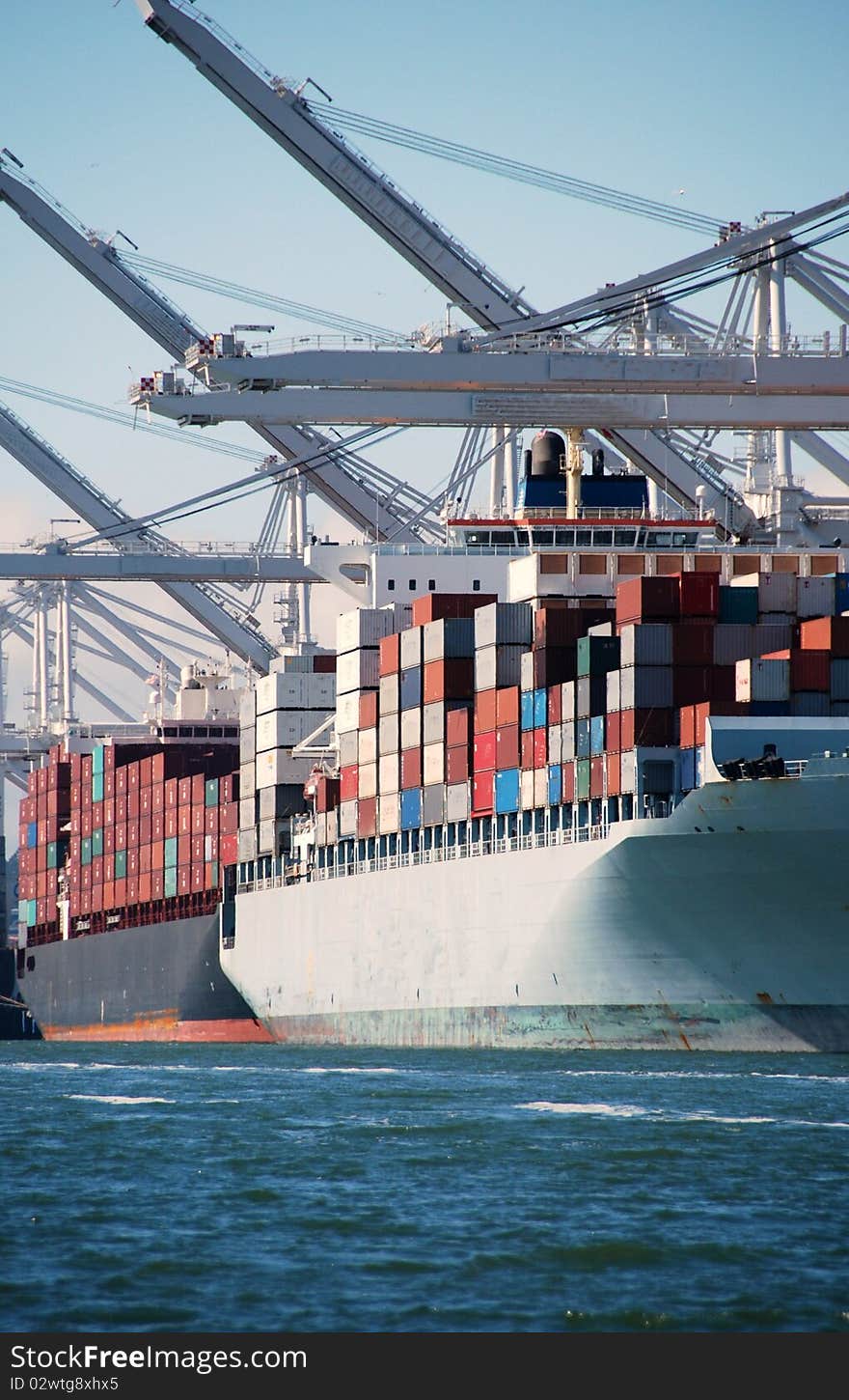 Two loaded freighters sit in port ready to cross the ocean and deliver goods. Two loaded freighters sit in port ready to cross the ocean and deliver goods