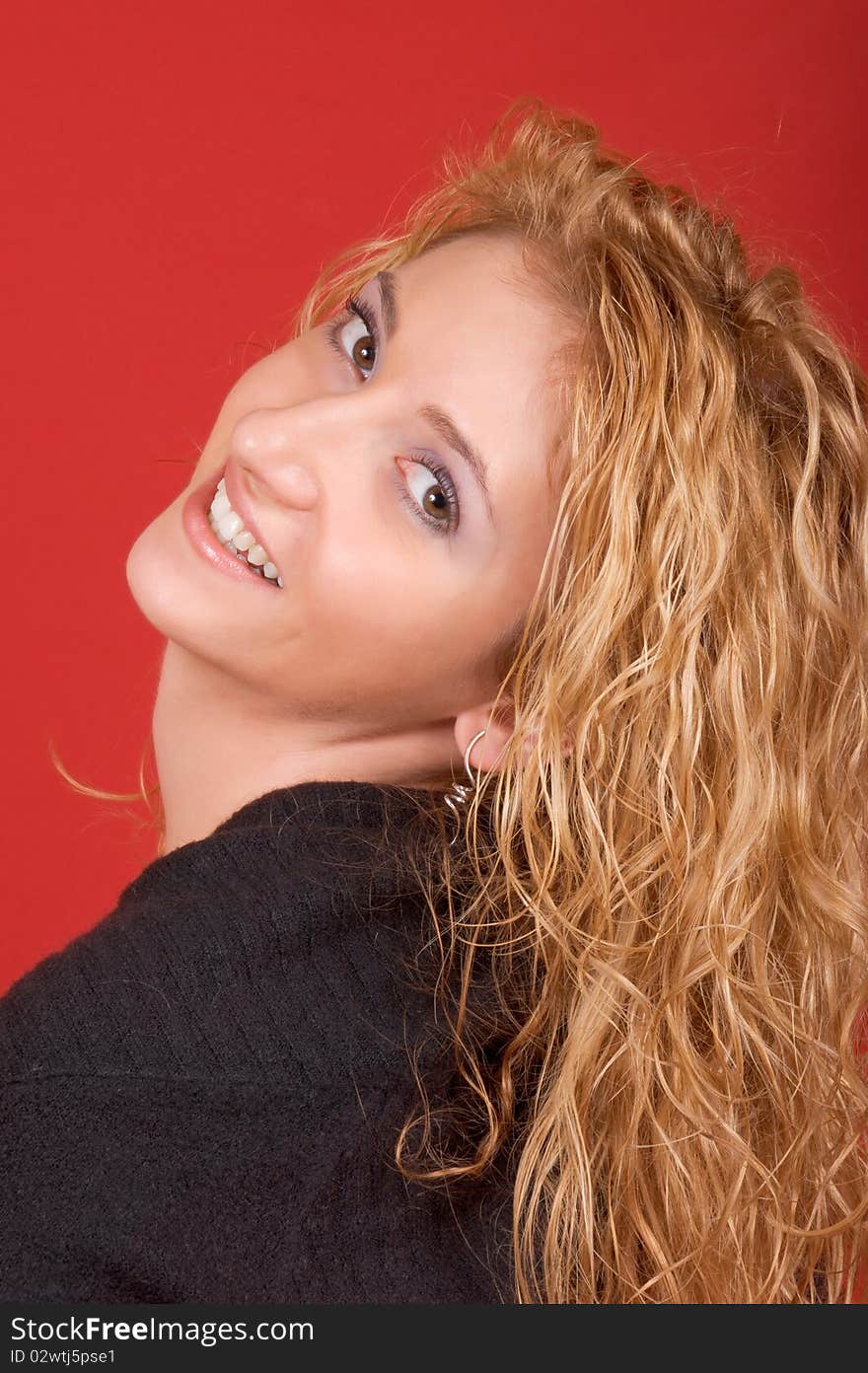 Beautiful young woman looking over shoulder and smiling. Studio shot over red background