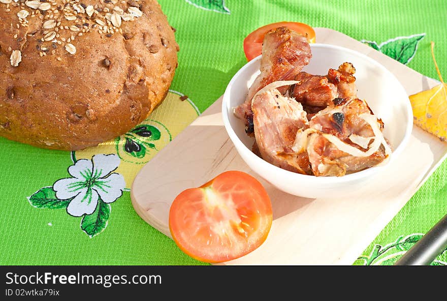 Grilled meat, tomatoes on the cutting board with loaf of rye bread. Grilled meat, tomatoes on the cutting board with loaf of rye bread