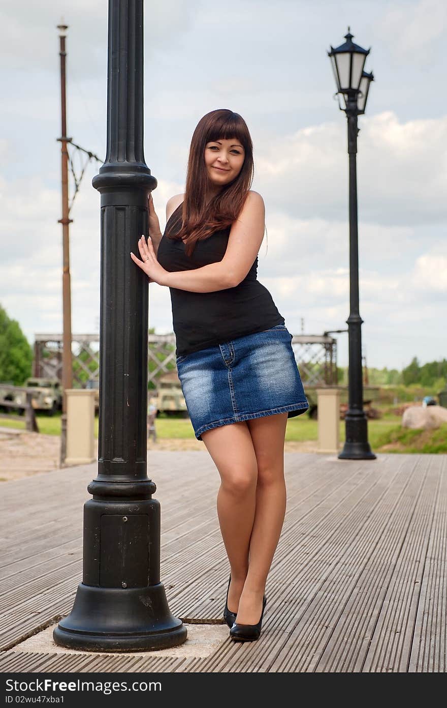 Young, woman in short skirt leans on lantern pillar. Young, woman in short skirt leans on lantern pillar.